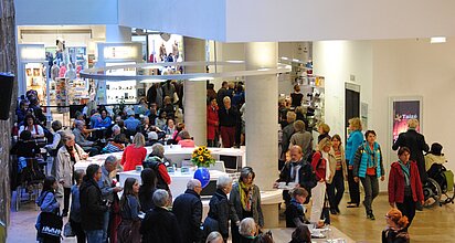 Viele Menschen bewegen sich rund um das Informationszentrum im Atrium
